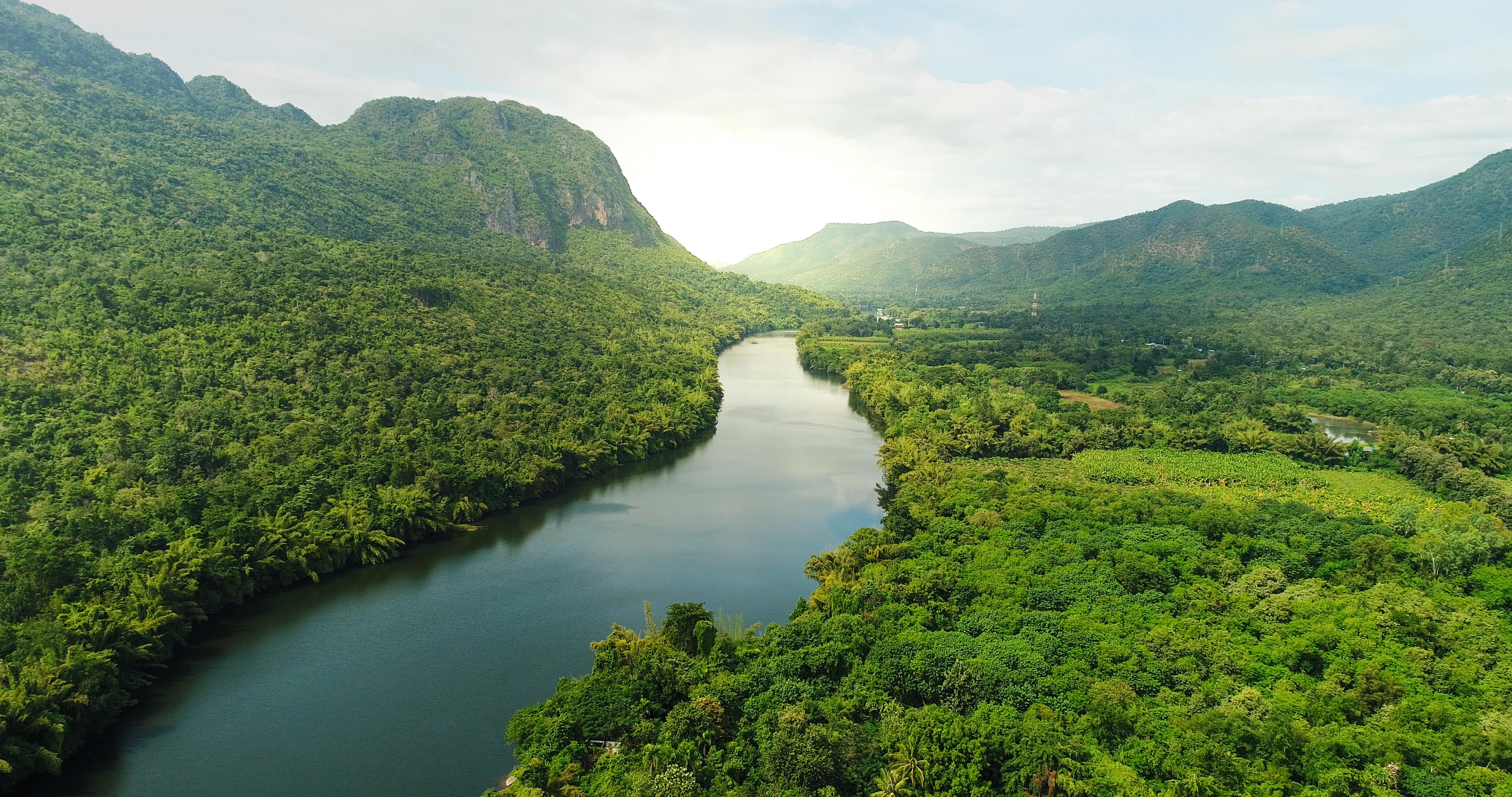 Beautiful natural scenery of river in southeast Asia. Tropical green forest with mountains in background, aerial view drone shot.