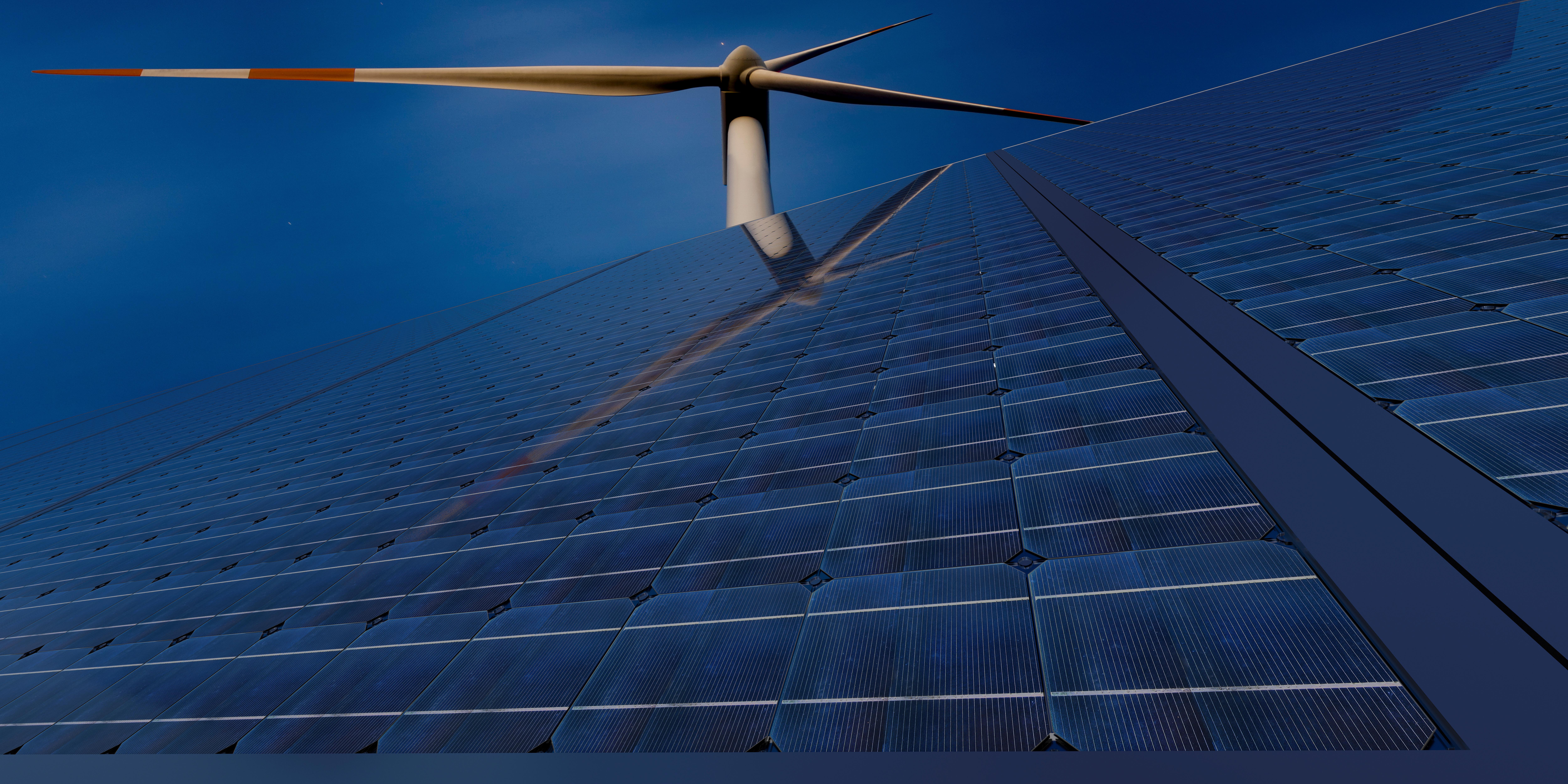 Blue solar panels freom a bottom angle with wind power in the back, pour L'ADOPTION DE L'ÉLECTRICITÉ RENOUVELABLE
