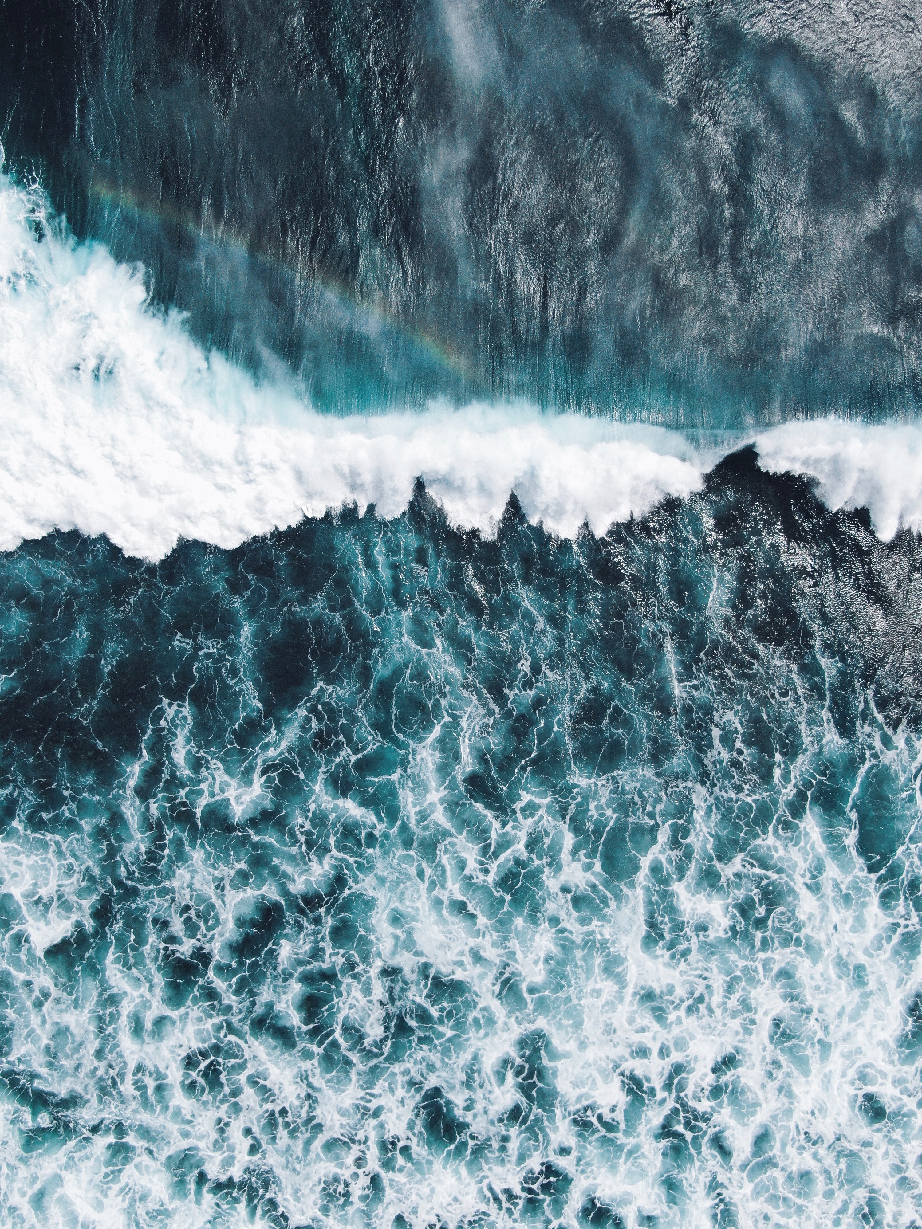 A top view of waves in the pacific ocean. Glimpse of a rainbow.
